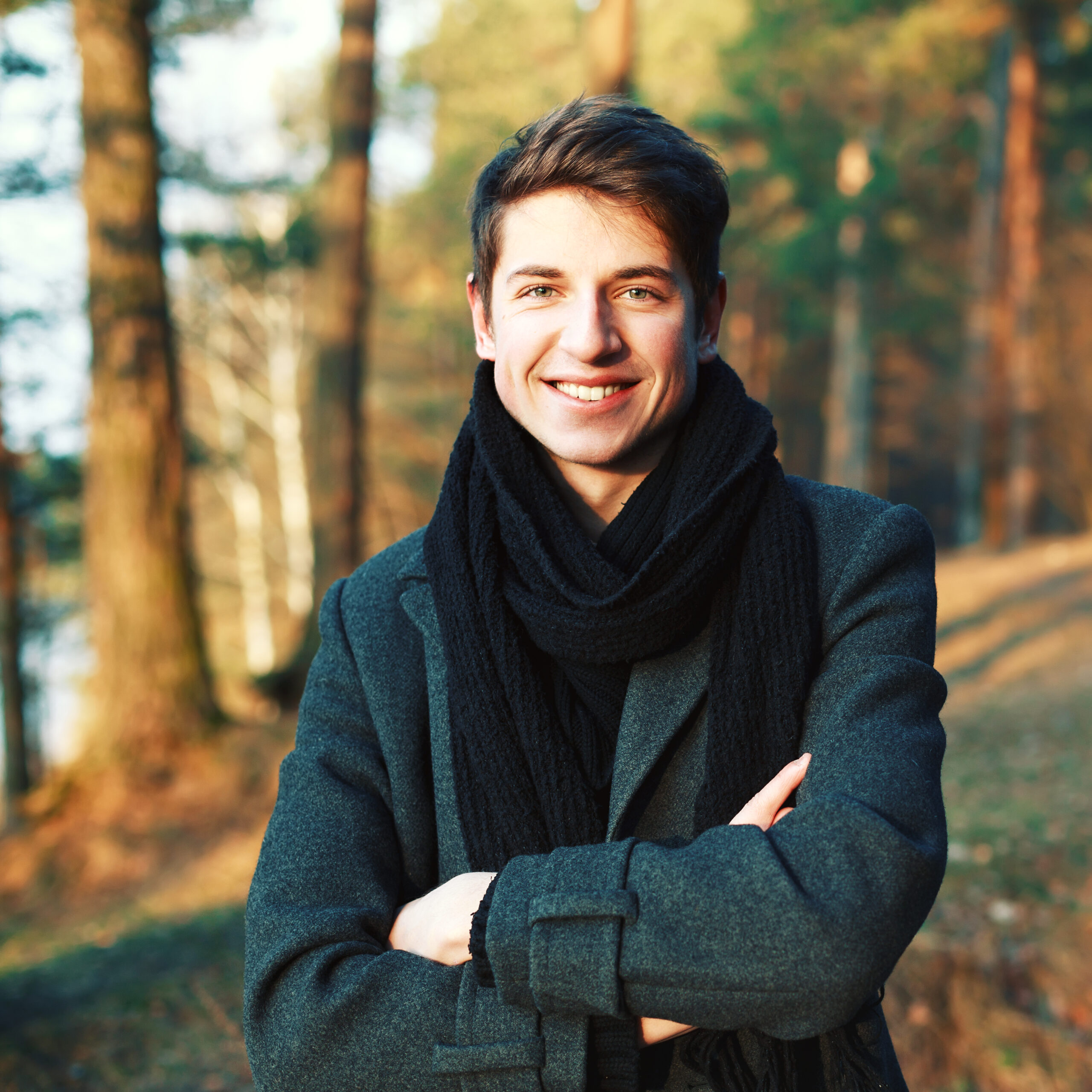 smiling young man with crossed arms outdoors